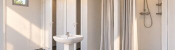 Interior de un módulo sanitario con cabinas de aseo, lavabo central y duchas separadas por cortinas.