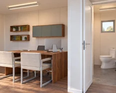 Visualización de una oficina modular con baño integrado, escritorio, dos sillas de visita y aseo independiente con lavabo e inodoro.